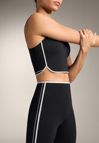 Black athletic crop top with white side stripes, featuring a fitted design and a scooped neckline, paired with high-waisted black leggings.