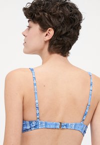 Blå blomstermønstret bikini topp med justerbare stropper og spenne bak. Stoffet har en glatt tekstur med levende farger.