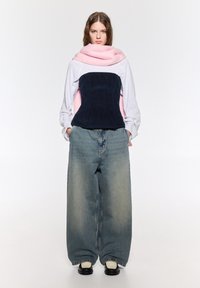 Överdimensionerade denimbyxor med en urtvättad finish, kombinerat med en lager-på-lager topp som har en rosa scarf och en mörkblå kordflorsbodice.