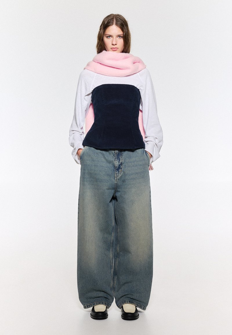 Överdimensionerade denimbyxor med en urtvättad finish, kombinerat med en lager-på-lager topp som har en rosa scarf och en mörkblå kordflorsbodice.