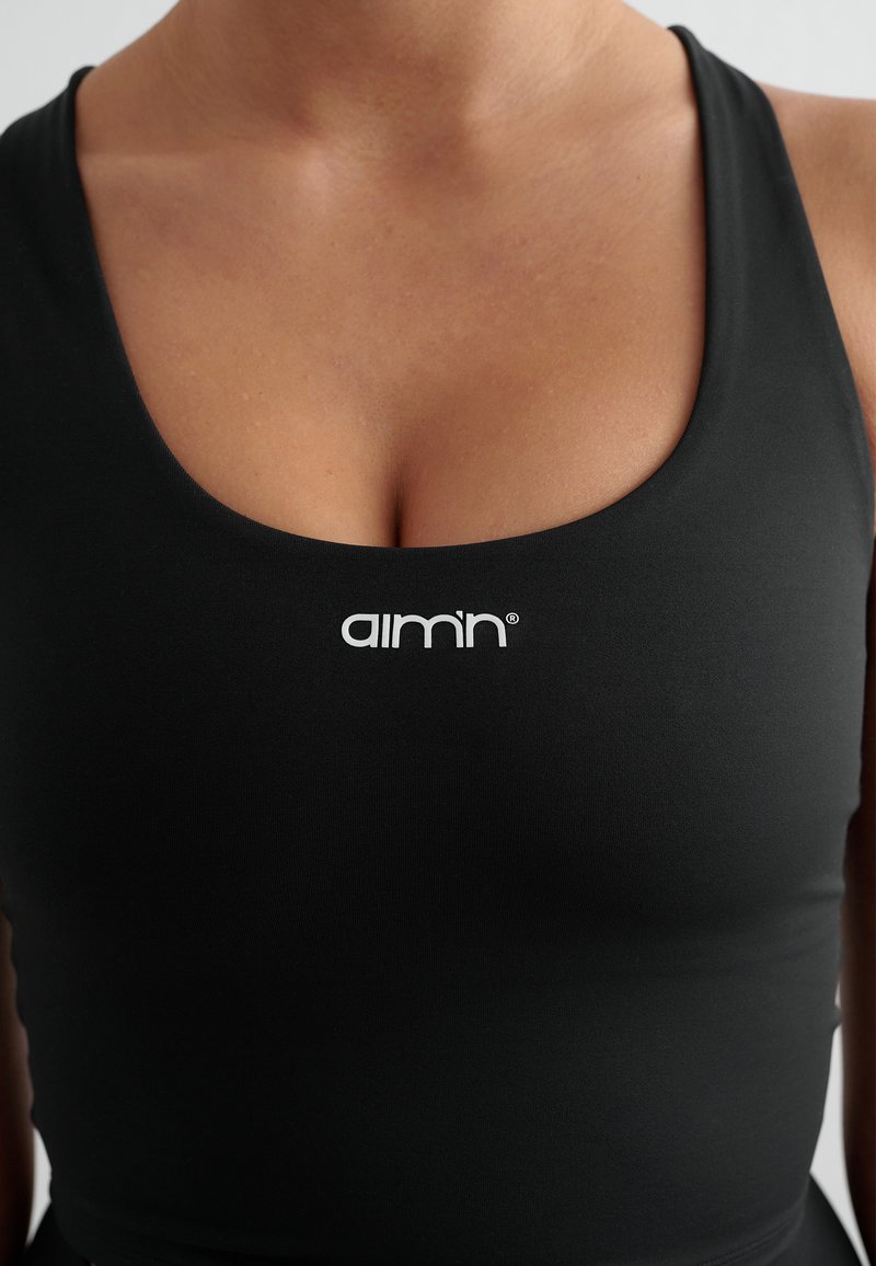 Svart sportslig tanktop med scoop hals, tettsittende design, og en hvit logo "aim’n" sentrert på brystet. Glatt tekstur.