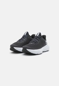 Zapatos deportivos negros con parte superior de malla transpirable, superficie texturizada, cordones y una sola acolchada blanca. Diseño a dos tonos con detalles de marca.