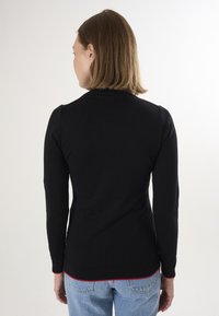 Zwarte langesluisse top met ronde hals, aansluitende siloet, geribbelde cuffs en een rode accent bij de zoom. Gladde textuur, minimalistisch ontwerp.
