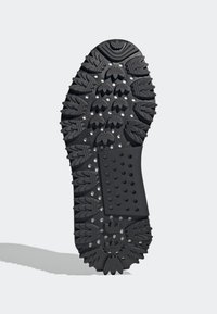 Svart gummisul med multidirektionellt mönster, som har spikar och cirkulära urtag för grepp och traction.