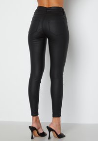 Zwarte high-waisted leggings van glanzend materiaal, met achterzakken en een slim fit, gecombineerd met open teen stiletto hakken.