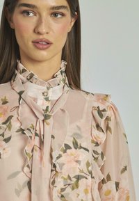 Blusa floreale in tessuto leggero di colore rosa chiaro. Collo e polsini a volant con stampa floreale in tonalità morbide di rosa e verde. Dettaglio dei bottoni sul collo.
