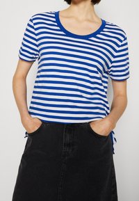 Camiseta de manga corta a rayas azules y blancas con cuello redondo, combinada con una falda de mezclilla negra de talle alto, que cuenta con bolsillos laterales.
