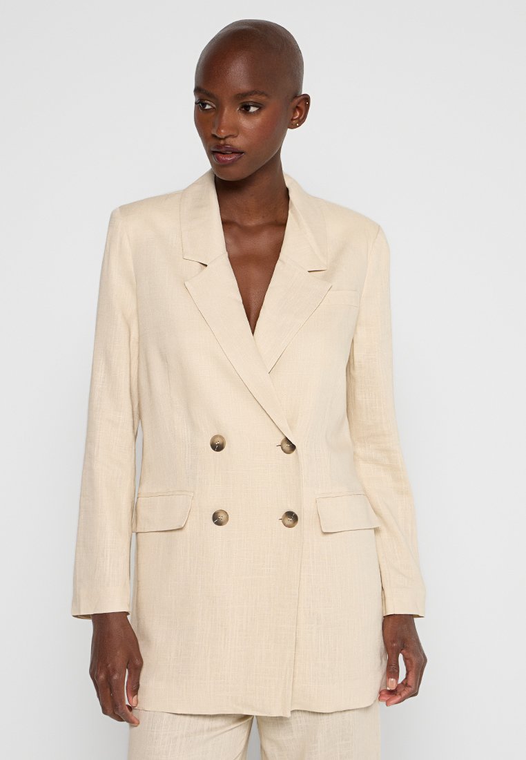 Hellbeige, doppelt geknöpfter Blazer aus strukturiertem Stoff, mit zwei Taschen an der Vorderseite und goldfarbenen Knöpfen. Maßgeschneiderter, strukturierter Schnitt.