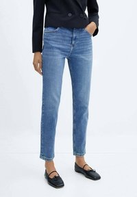 Vaqueros de mezclilla azul claro con corte recto, talle alto y un sutil desgaste, combinados con bailarinas negras y un blazer negro.