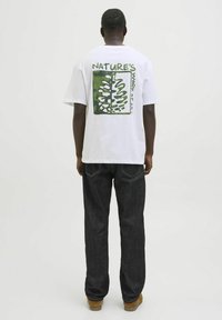 Hvid bomulds t-shirt med et grønt og sort grafisk design på ryggen, der har et bladmønster og teksten: "NATURE'S WORK of ART."