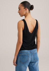 Top a fascia nera con scollatura a V profonda, caratterizzato da un motivo zigzag testurizzato, abbinato a jeans alta vita di colore azzurro chiaro.