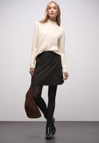 Neulottu norsunluunvärinen paita, jossa korkea kaulus; tumma ruudullinen hame; mustat sukkahousut; mustat nilkkurit; ruskea mokkanahkainen olkalaukku.