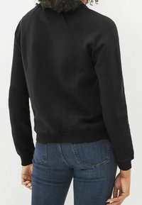 Schwarzer Sweatshirt mit geripptem Saum und Bündchen, abgerundetem Halsausschnitt und Raglanärmeln. Glatte Textur, minimales Design, keine sichtbaren Logos.