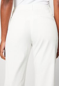 Vita tygbyxor med rak benstil, som har två bakfickor och en slät textur. Midjebandet sitter bekvämt vid höfterna.