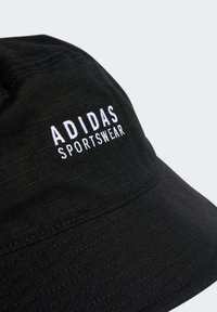 Chapeau de seau noir en tissu texturé, avec une broderie blanche "ADIDAS SPORTSWEAR" sur le côté et un design de bord incurvé simple.