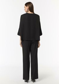 Black, loose-fitting outfit featuring a wide, draped top and wide-leg pants. The fabric appears smooth with a lightweight texture.