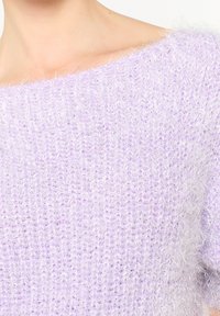 Vaaleanliila neulepaita, jossa on rento istuvuus, teksturoitu kangas ja pehmeä, pörröinen pinta. Sissä on leveä, olkapäiltä avonainen kaula-aukko.