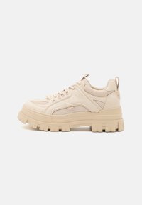 Zapatillas beige con suela gruesa, parte superior de malla y ante, sistema de cordones pronunciado y una pequeña etiqueta en el talón.