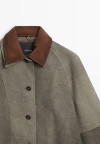 Giacca in suede grigia con colletto marrone scuro e chiusura a bottoni, mostrante la parte superiore e l'etichetta del marchio all'interno del colletto.