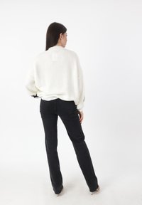 Oversized witte geribde trui met wijde mouwen, gecombineerd met zwarte skinny jeans. Eenvoudig, textuurontwerp, geen patronen of opvallende details.