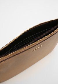 Hnědá kožená zipová taštička se zlatým zipem a malými zlatými písmeny, ukazující vnitřní černou podšívku a oddíly.