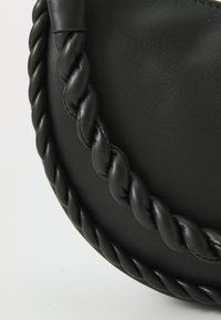 Sac en cuir noir avec une poignée tressée, présentant une texture lisse et une forme arrondie. Détails notables : un accent doré.