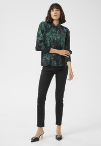 Black button-up shirt with green floral pattern, long sleeves, and smocked cuffs, paired with black skinny jeans and pointed black heels.