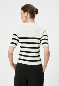 Weißes, geripptes Strick-Polohemd mit schwarzen horizontalen Streifen, kurzärmelig und tailliert. Die Rückseite hat einen klassischen Polo-Kragen.