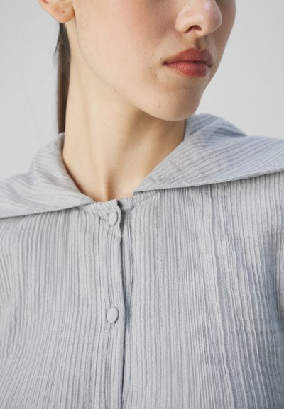 Light gray, textured top with vertical ribbing and a hood. Features two round buttons at the neckline, creating a layered appearance.