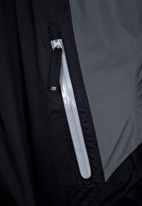 Černá a šedá tkanina s kapsou na zip. Zip je stříbrný, s textilním táhlem. Hladký povrch, lehký materiál.