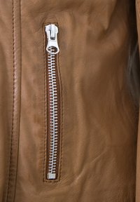 Braune Lederjacke mit einem silbernen Reißverschluss auf der linken Seite, sichtbaren Nähten und einer strukturierten Oberfläche.