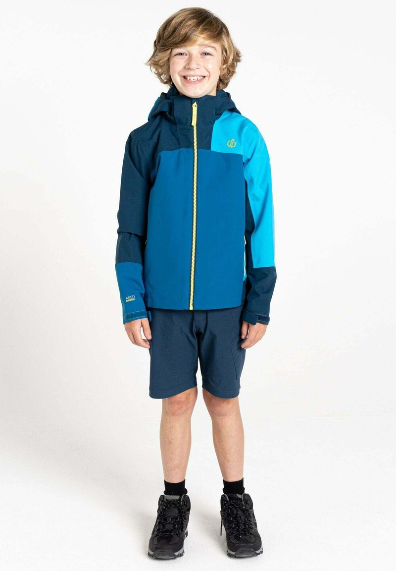 Blaue und türkise Jacke mit einem Reißverschluss vorne und Kapuze, kombiniert mit dunklen Shorts und schwarzen Wanderstiefeln. Glattes Material mit kontrastierenden Akzenten.