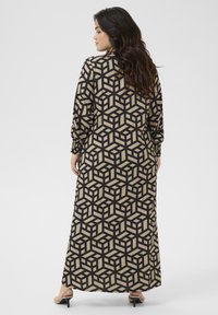 Maxikleid in Beige mit einem geometrischen schwarzen Würfelmuster. Lange Ärmel mit gerafften Manschetten und einem lockeren Schnitt. Weicher Stoff.