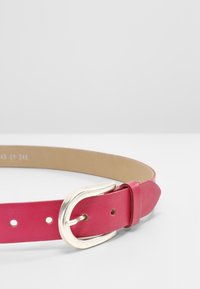 Rosa Leder-Gürtel mit einer silbernen Metallschnalle, flacher Form und sichtbaren Löchern zur Anpassung. Glatte Textur mit einem klaren Design.