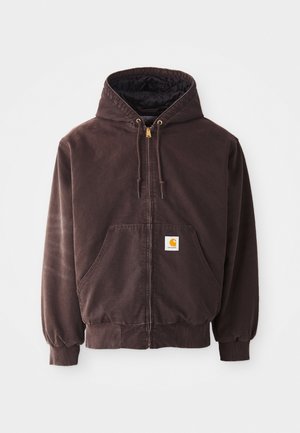 Brūns zip-up džemperis ar kapuci, divām priekšējām kabatām, ribotiem cimdotēm un apakšmalu. Iespējas ar zeltainiem aukliņu galiem un balto logotipa uzlīmi uz kabatas.