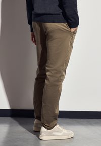 Beige puuvillapantsut, millel on kitsas sobivus ja küljetaskud, koos heledate tossudega. Materjal on sileda tekstuuriga.