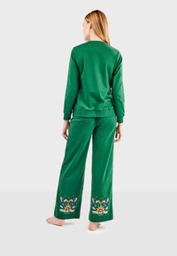 Zeleni loungewear set koji se sastoji od majice s okruglim izrezom i hlača širokih nogavica s dekorativnim printom na rubovima hlača. Mekani pamučni materijal.