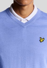 Maglione a maniche corte azzurro chiaro con scollatura a V. Presenta un piccolo logo di un uccellino giallo ricamato sull'area del petto sinistro. Tessuto testurizzato.