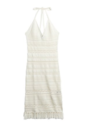 Robe tricotée blanche avec un décolleté en V, bretelles halter et motifs texturés complexes. Présente un ourlet à franges et des détails ajourés.