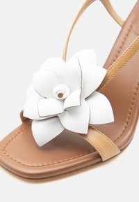 Ταμπά δερμάτινο σανδάλι με τετράγωνη μύτη και μπεζ λουράκι, διακοσμημένο με μεγάλο λουλούδι από λευκό δέρμα μπροστά.