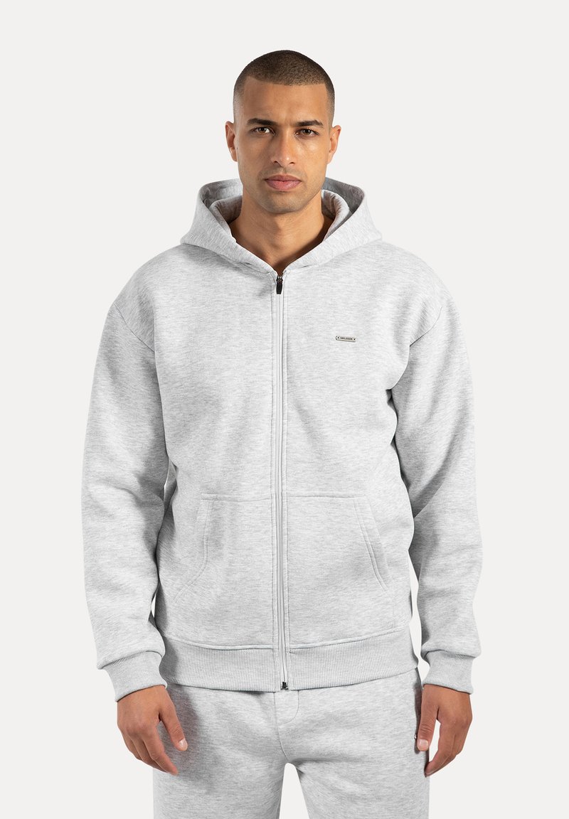 Chaqueta con cremallera gris hecha de tejido suave, con capucha, grandes bolsillos frontales, puños acanalados y un pequeño logo en el pecho.