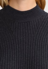 Pull à côtes gris foncé avec un col montant et des détails texturés sur les épaules et les côtés. Tissu doux avec des lignes verticales.