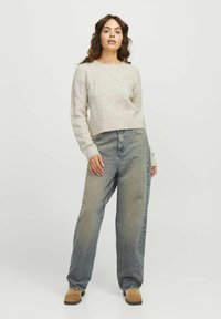 Maglione lavorato a maglia grigio chiaro con un motivo a diamante testurizzato, abbinato a jeans blu chiaro a vestibilità comoda e scarpe slipper marroni.