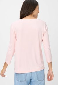 Helles rosa Langarmshirt mit rundem Halsausschnitt, seitlichen Schlitzen und glattem, weichem Stoff, kombiniert mit hellblauen Jeans.