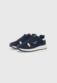 Mørkeblå sneakers med en kombination af mesh og fløjlmateriale. Har hvide detaljer, rød pynt på bagsiden og en tekstureret gummisål.