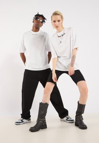 Hvide oversized t-shirts med "New York" trykt, parret med sorte shorts og varieret fodtøj: chunky sorte støvler og sportsko.