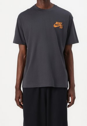 Dunkelgraues Baumwoll-T-Shirt mit rundem Ausschnitt und kurzen Ärmeln, versehen mit einem orangefarbenen Nike SB-Logo auf der linken Brust.
