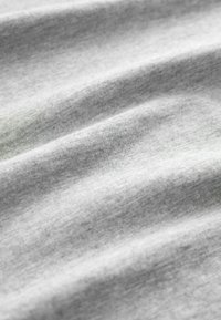 Svetlošedá látka s hladkým povrchom, ktorá zobrazuje jemné vlnky a variácie v odtieňoch, pričom naznačuje mäkký materiál z bavlnenej zmesi.