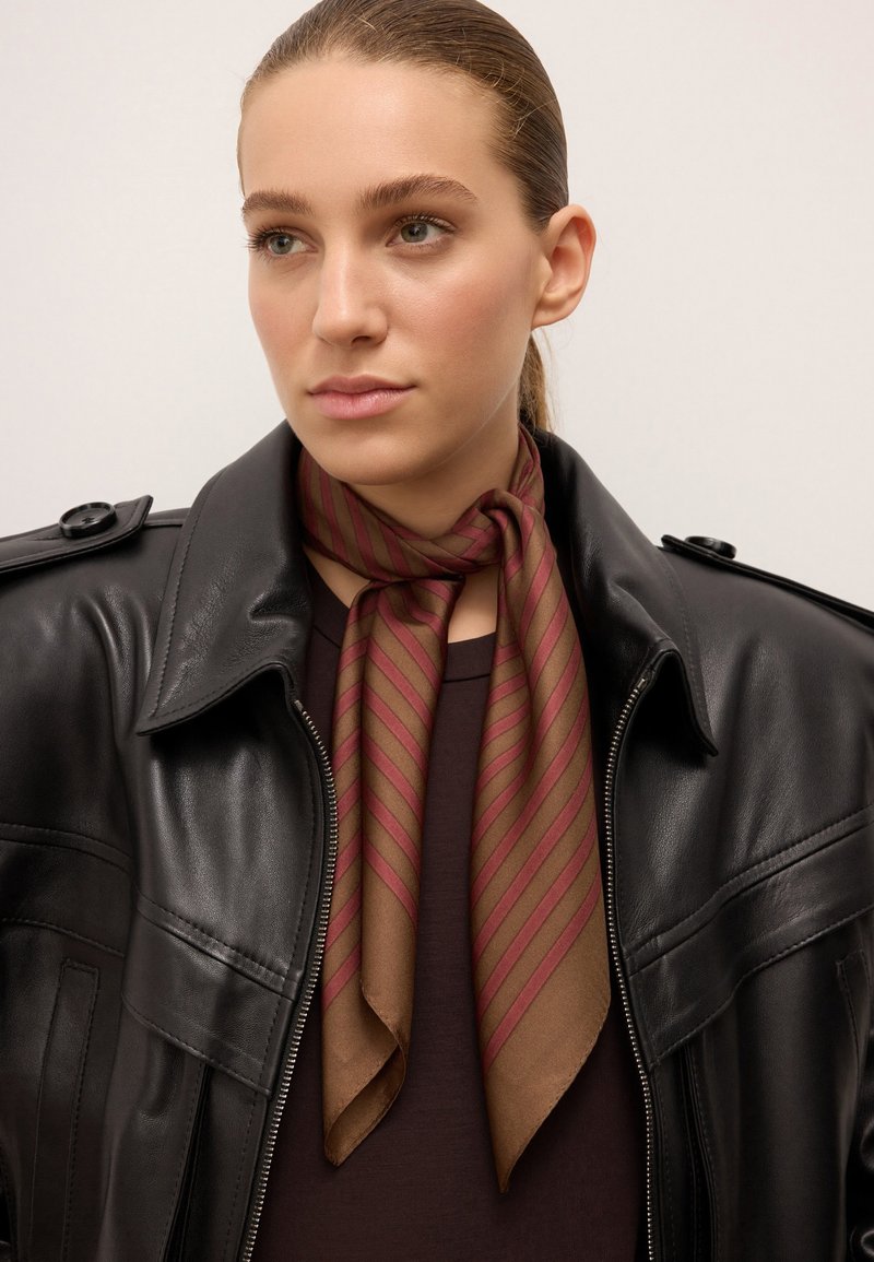 Écharpe rayée marron et bordeaux nouée autour du cou, associée à une veste en cuir noire et un haut sombre, mettant en valeur des textures lisses et des couleurs contrastées.