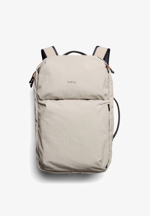 Zaino beige chiaro con una morbida texture in tessuto, cerniere e manico superiore. Dotato di spallacci imbottiti e un logo del marchio discreto sulla parte anteriore.